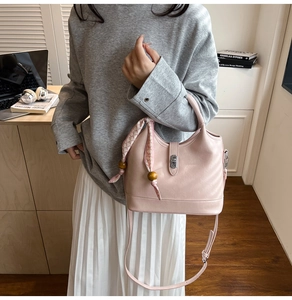 Détail du sac seau rose en cuir avec foulard décoratif et breloques en bois au bureau