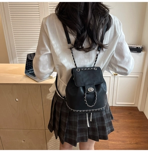 Detail of a black faux leather backpack with silver chains shown in a casual home setting