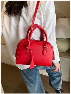 Detailed view of a red leather Boston bag featuring top handles and adjustable shoulder strap