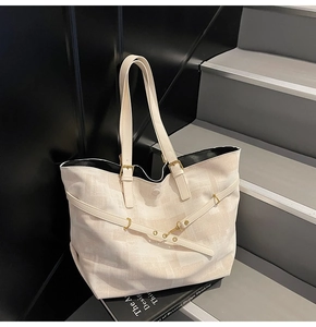 Detail view of large cream tote bag featuring adjustable leather straps and metal hardware