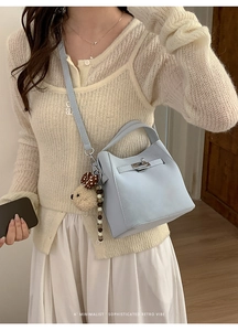 Close-up of light blue leather bucket bag with metal turn-lock and cute bear charm