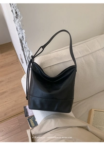 Minimalist black hobo shoulder bag with a sleek retro vibe on a white sofa backdrop