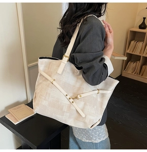 Macro detail of beige textured tote bag showing white leather straps and golden metal hardware
