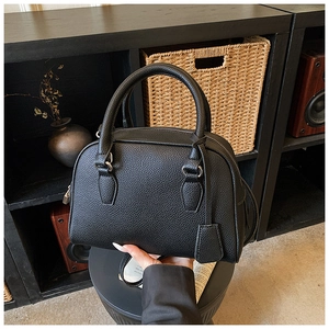 Close-up of black lychee grain leather boston bag with top handles on display base