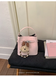 Close-up of pink leather bucket bag featuring a gold twist lock and a cute puppy plush charm
