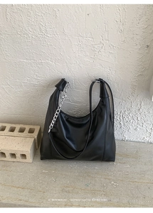 Detail of minimalist black leather hobo bag with bold silver metal chain and soft textures
