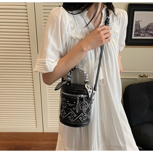 Model wearing a black cylindrical bucket bag with geometric patterns and a silk scarf strap