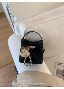 Detail of black suede bucket bag with metal lock, woven strap and plush bear charm