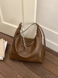 Minimalist brown hobo tote bag with silver chain strap on a vintage wooden floor
