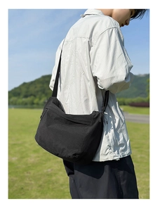 Outdoor close-up of a black nylon crossbody bag with adjustable strap and side zipper