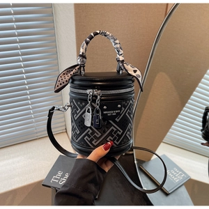 Close-up of black barrel bag featuring geometric texture and elegant silk scarf handle decoration