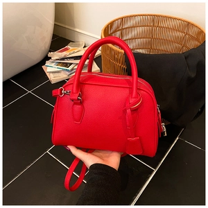 Red lychee grain Boston bag with dual handles and metal lock detail shown in a home setting