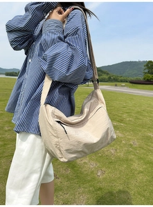 Outdoor shot of beige nylon crossbody bag with adjustable wide strap and side zipper