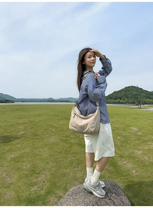 Outdoor view of a beige large nylon crossbody dumpling bag with durable zipper details