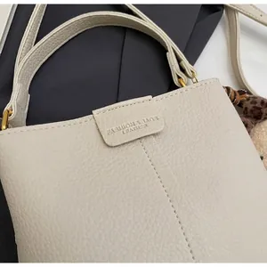 Detail of off-white lychee grain leather handbag with gold buckle and leopard pompom