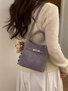 Elegant purple bucket bag with silver lock and teddy bear charm shown in a lifestyle pose