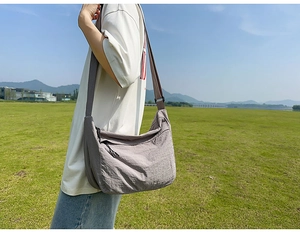 Outdoor model shot of a large capacity purple nylon crossbody bag with adjustable strap