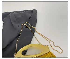 Close-up of golden metallic evening clutch with sleek snake chain on a grey blazer