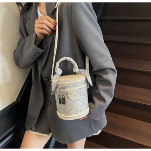 Detail of cream bucket bag with monogram pattern and silk scarf handle on model