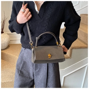 Close-up of a grey leather crossbody bag with a golden metal twist-lock and top handle