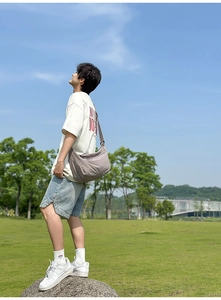 Outdoor view of a neutral grey nylon crossbody bag shown in a casual urban lifestyle setting