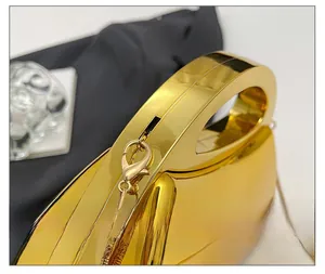 Close-up of shiny gold acrylic evening bag featuring arc handle and metal chain link