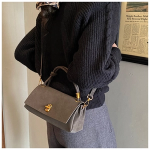 Détail du sac en cuir gris mat avec fermoir doré porté par un mannequin en tricot