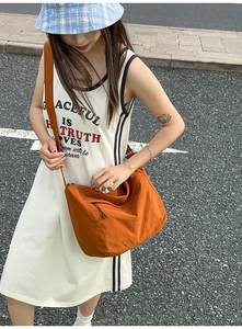 Detail of a large orange nylon crossbody bag with zipper and wide adjustable shoulder strap