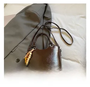 Détails du sac seau en cuir brillant marron foncé avec un charm perlé et une bandoulière