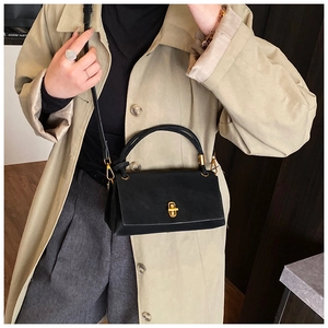 Close-up of elegant black faux leather handbag with shiny gold twist-lock closure detail