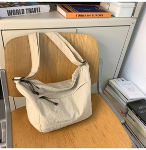 Detail of a cream nylon crossbody bag with zipper pockets and a textured finish