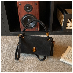 Detail showing matte black suede surface and elegant gold twist lock on the handbag