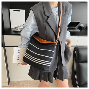 Detail of navy striped canvas bucket bag with brown leather trim and adjustable strap
