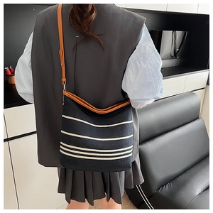 Detail of navy canvas bucket bag with beige stripes and brown leather strap on model