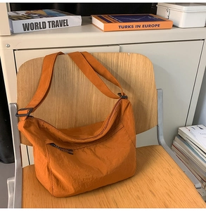 Detail of orange nylon dumpling bag with adjustable strap on a wooden chair