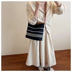 Detail view of black canvas bucket bag with white stripes and brown leather strap