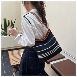 Detail of striped canvas bucket bag with brown leather straps and spacious interior