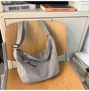 Detailed shot of grey textured nylon crossbody bag with adjustable black strap on a chair