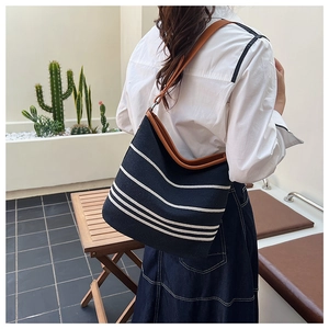 Detail of black striped canvas tote bag with brown leather straps on woman's shoulder