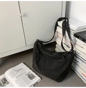 Minimalist black nylon crossbody bag with zipper detail on a scholarly book background