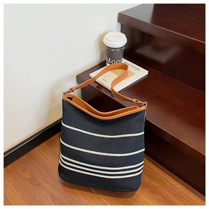 Detail of black and white striped canvas bucket bag with adjustable brown leather strap
