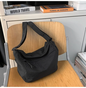 Detail view of black nylon crossbody bag hanging on a chair with side zipper pocket