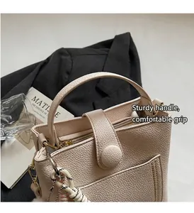 Détail du sac seau blanc crème avec motif litchi et pendentif décoratif tressé
