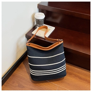 Close-up of black canvas tote bag with white stripes and brown leather strap on wooden steps