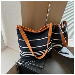 Detail of striped canvas bucket bag showing brown leather trim and adjustable shoulder strap