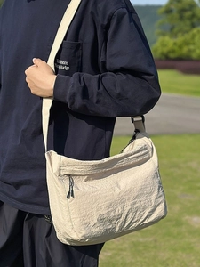 Off-white nylon crossbody bag with adjustable strap shown on model in park setting