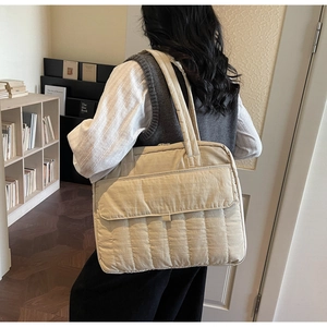 Detail der beigen Stepptasche mit gepolsterter Textur und großer Frontklappentasche