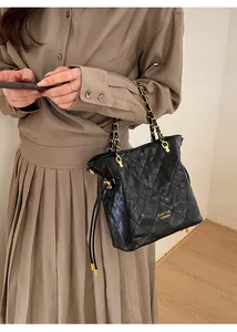 Gros plan d'un sac seau matelassé noir avec bandoulière chaîne dorée et logo doré