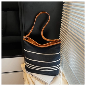 Detail of striped canvas bucket bag with brown leather straps under blinds sunlight