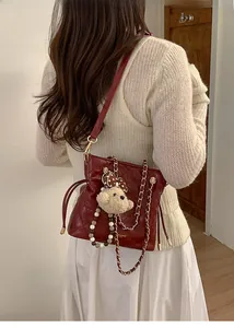 Detail of burgundy quilted bucket bag with pearl strap and teddy charm accessory